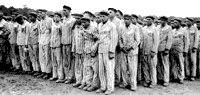 Prisoners standing for roll call at the Buchenwald concentration camp in Germany, circa 1938. This twice-daily ordeal of several hours in all weather was so the SS guards could account for every single prisoner. Roll calls of many hours' duration were used also as camp-wide punishment, often ending in death for the weakest. The prisoners' uniforms bear classifying triangular badges and identification numbers. Homosexual prisoners were identified by pink triangle badges.