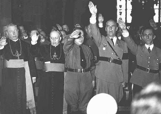 Catholic clergy and Nazi officials, including Joseph Goebbels (far right) and Wilhelm Frick (second from right), give the Nazi salute. Germany, date uncertain.