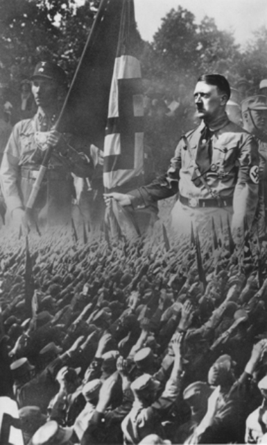 Postal fotográfica en la que puede verse la imagen de una multitud de alemanes saludando superpuesta a una imagen ampliada de Hitler y de un soldado de asalto. Munich, Alemania, aproximadamente en 1932.