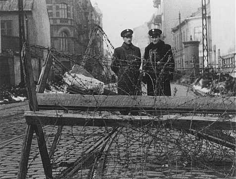Poliziotti ebrei presidiano una delle entrate del ghetto di Varsavia, ostruita da filo spinato. Polonia, febbraio 1941.