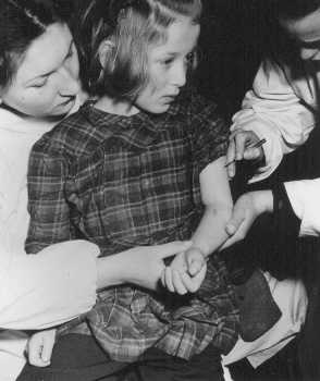 Equipe das Nações Unidas vacina uma sobrevivente de 11 anos que foi vítima de experiências médicas no campo de concentração de Auschwitz. Campo de deslocados de guerra de Bergen-Belsen, Alemanha, maio de 1946.
