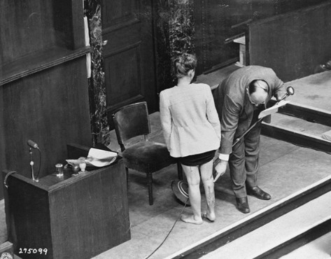 A sobrevivente do campo de concentração Jadwiga Dzido mostra a perna com cicatrizes para a Corte de Nuremberg enquanto um médico explica a natureza dos procedimentos infligidos nela no campo de concentração de Ravensbrück em 22 de novembro de 1942. As experiências médicas, incluindo injeções de bactérias altamente potentes, foram realizadas pelos réus Herta Oberheuser e Fritz Ernst Fischer. 20 de dezembro de 1946.