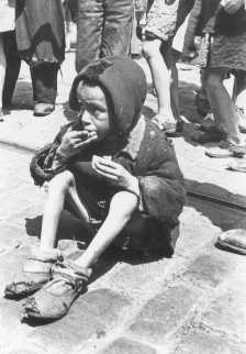 Criança emaciada comendo algo nas ruas do Gueto de Varsóvia. Varsóvia, Polônia.  Foto tirada entre 1940 e 1943.