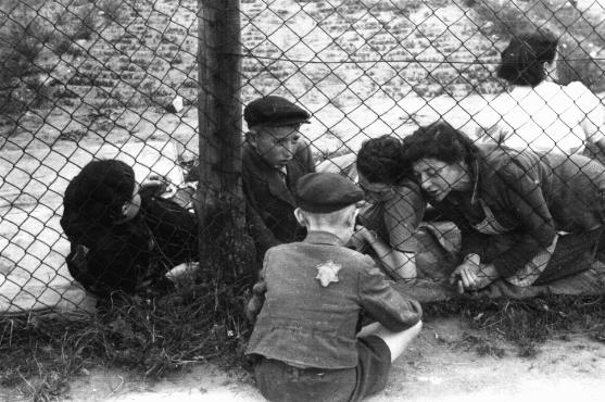 Family members say goodbye to a child through a fence at the ghetto's central prison where children, the sick, and the elderly were held before deportation to Chelmno during the 
