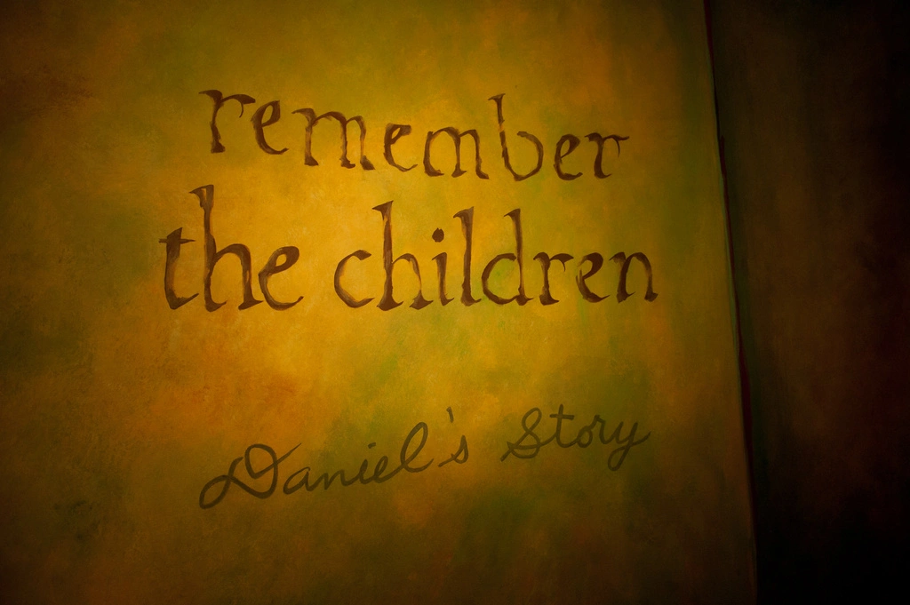 A yellow poster, the main title in large, lower cased letters says "remember the children." Below that is the subtitle in cursive, "Daniel's Story"