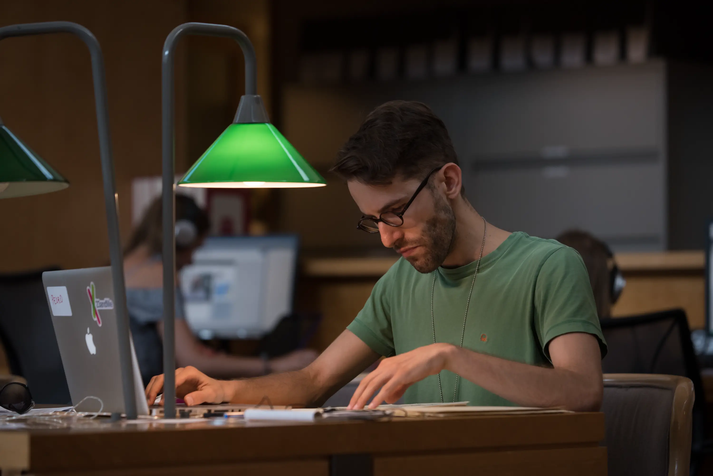 A person in a library, sitting at a desk reviewing their notepad next to a laptop