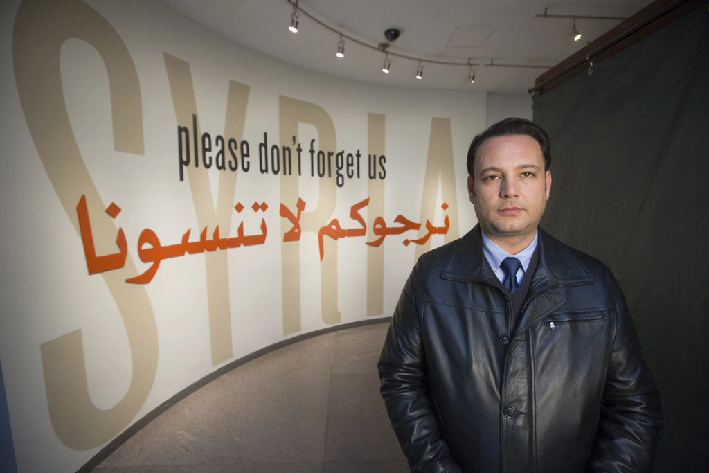 A Syrian man stands in front of the Museum's Syria exhibit , with the title "please don't forget us" in English and Arabic