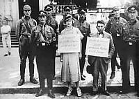 This photograph shows the public humiliation of a couple. The woman, who is non-Jewish, carries a sign reading “I am the greatest swine and sleep only with Jews.” The man's sign reads, “As a Jew, I only take German girls up to my room.”