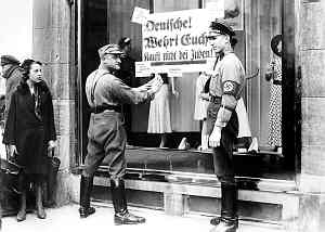 Nazi leaders organized a nationwide boycott of Jewish stores on April 1, 1933. In this photograph, a passerby looks on as a Nazi Storm Trooper plasters a display window with signs urging German citizens not to buy from Jews.