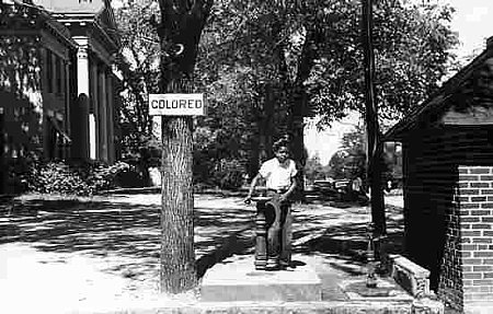 This photograph was taken in Halifax, North Carolina (U.S.), in April 1938. The sign on the tree (“Colored”) indicates that the water fountain was for use by Blacks, who were forbidden to use fountains reserved for white people. This photograph was taken in Halifax, North Carolina (U.S.), in April 1938. The sign on the tree (“Colored”) indicates that the water fountain was for use by Blacks, who were forbidden to use fountains reserved for white people.